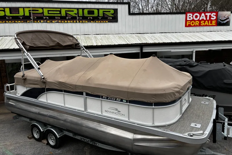 Slide: The Image of 2023 Bennington 23 SSR S pontoon boat with cover at dealership, boats for sale sign visible. - 3
