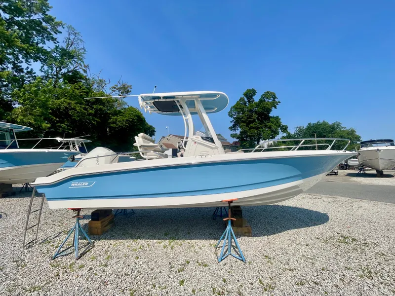 Slide: The Image of A Boston Whaler 220 Dauntless boat is on a gravel lot, surrounded by trees and other boats. - 1