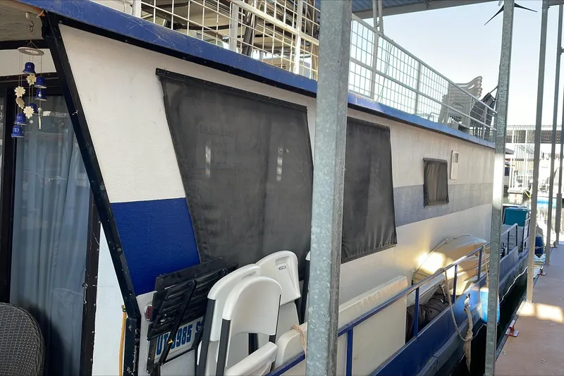 Slide: The Image of 1986 Boatel Hercules houseboat docked, featuring blue and white exterior with covered windows. - 6