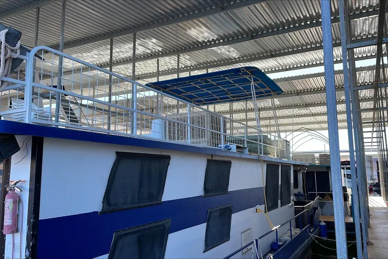 Slide: The Image of 1986 Boatel Hercules houseboat docked under a metal canopy, featuring a blue and white exterior. - 9