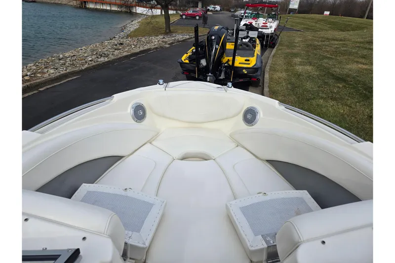 Slide: The Image of 2009 Bayliner 225 boat interior with white seating, parked near a lakeside. - 18
