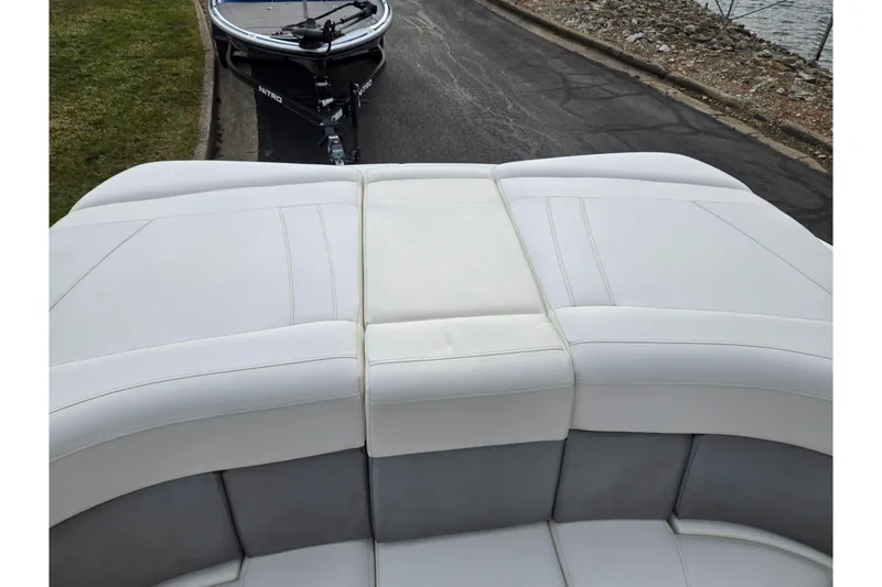 Slide: The Image of 2009 Bayliner 225 boat with white cushioned seating, parked near a lake. - 23