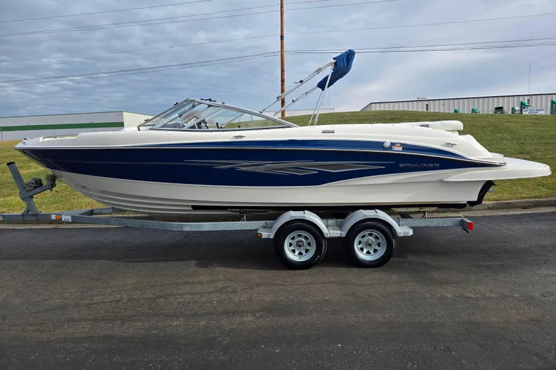 Slide: The Image of 2009 Bayliner 225 boat on trailer, blue and white design, parked outdoors. - 4