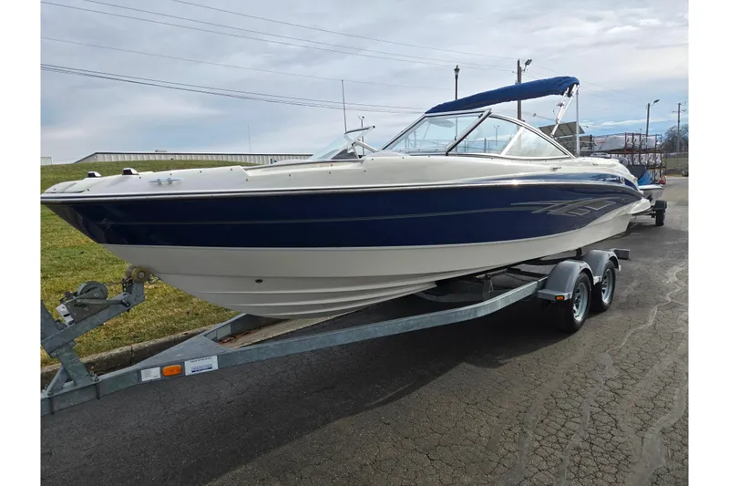 Slide: The Image of 2009 Bayliner 225 boat on trailer, blue and white, parked outdoors. - 5