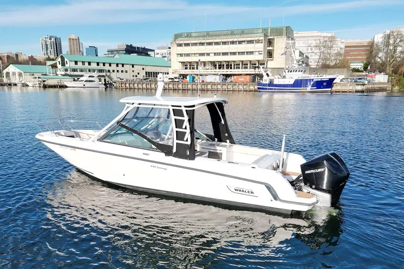 Slide: The Image of 2019 Boston Whaler 270 Vantage boat on water near urban marina backdrop. - 8