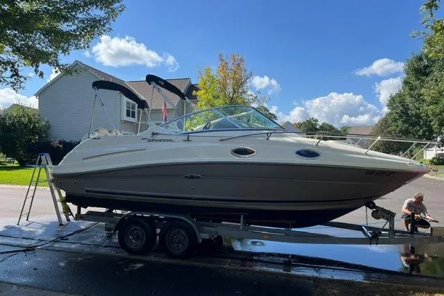 Slide: The Image of 2008 Sea Ray 240 Sundancer boat on trailer, parked in residential area under clear blue sky. - 4