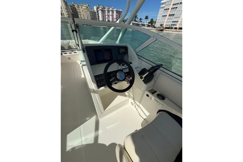 Slide: The Image of 2017 World Cat 230 SD boat helm with steering wheel and controls, docked near waterfront buildings. - 13