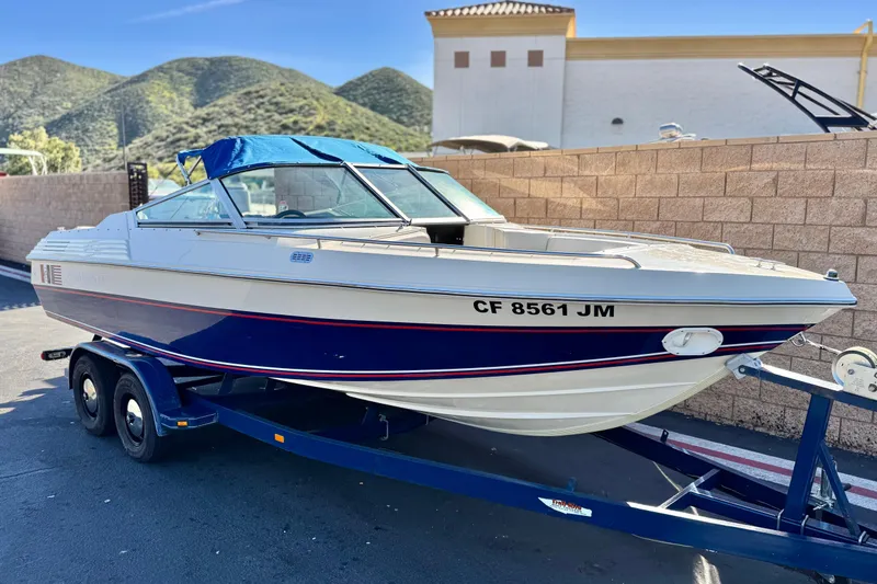 Slide: The Image of 1988 Cobalt 222 boat on trailer, parked outdoors with scenic mountain backdrop. - 1