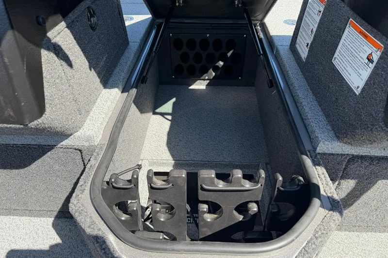 Slide: The Image of Storage compartment of 2026 Lund 1875 Pro-V boat, featuring rod holders and safety instructions. - 16