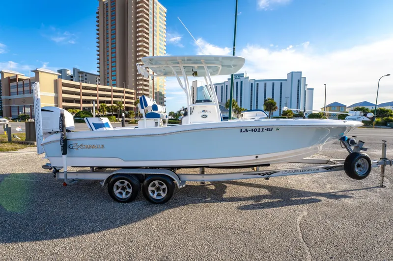 Slide: The Image of 2017 Crevalle 26 Open boat on trailer, parked near tall buildings under blue sky. - 3
