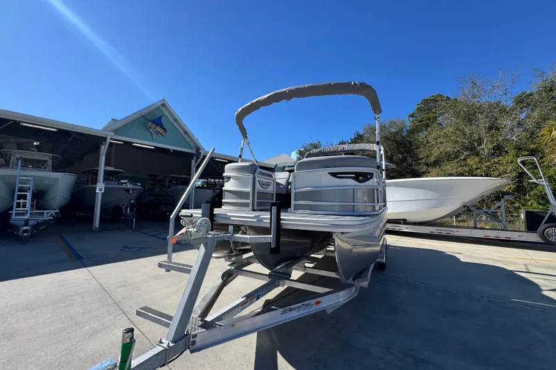 Slide: The Image of 2026 Bennington 23 MFB pontoon boat on trailer, parked outdoors under clear blue sky. - 5