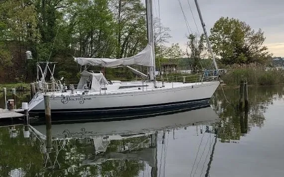 The Image of 1985 Beneteau First 42 sailboat docked by a calm riverbank. - 0