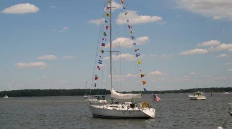 Slide: The Image of 1985 Beneteau First 42 sailboat with flags on calm water. - 2