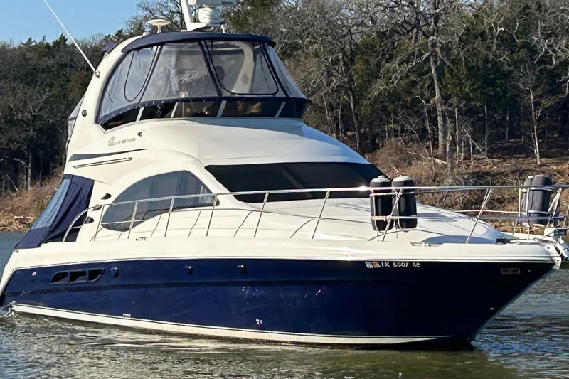 The Image of 2005 Sea Ray 44 Sedan Bridge yacht on a calm lake, surrounded by trees. - 0