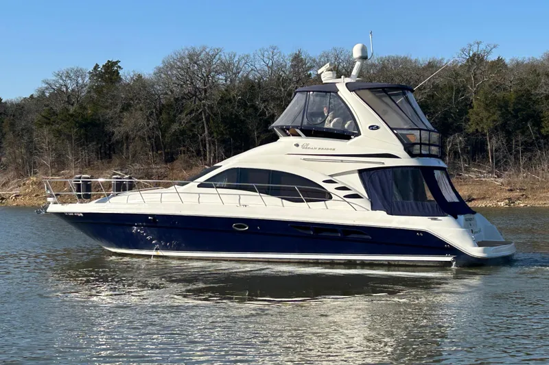 Slide: The Image of 2005 Sea Ray 44 Sedan Bridge yacht cruising on a calm lake with forested shoreline. - 55