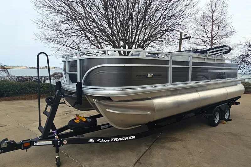 The Image of 2026 Sun Tracker Fishin' Barge 22 XP3 pontoon boat on trailer, parked near waterfront. - 0