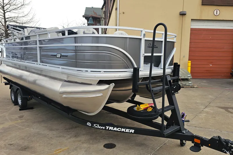 Slide: The Image of 2026 Sun Tracker Fishin' Barge 22 XP3 pontoon boat on trailer, parked outdoors. - 5
