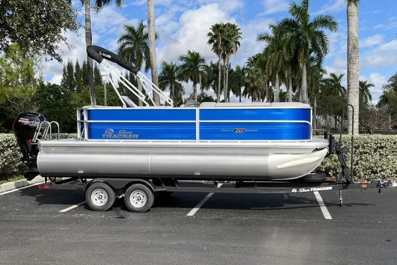 Slide: The Image of 2026 Sun Tracker Party Barge 20 DLX pontoon boat on trailer, parked with palm trees. - 94