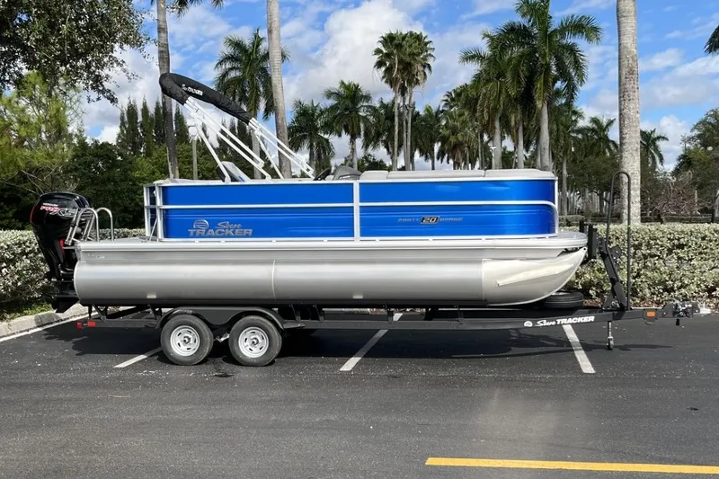 Slide: The Image of 2026 Sun Tracker Party Barge 20 DLX pontoon boat on trailer, parked with palm trees. - 95