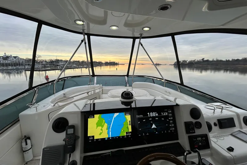 Slide: The Image of 2008 Sea Ray 52 Sedan Bridge helm with navigation screens, overlooking serene waters at sunset. - 7