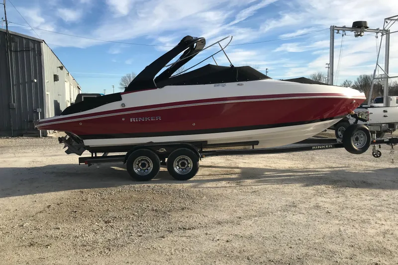 The Image of 2018 Rinker QX26 BR boat on trailer, red and white design, parked outdoors. - 1