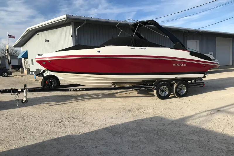 Slide: The Image of 2018 Rinker QX26 BR boat on trailer, red and white, parked outside a building. - 10