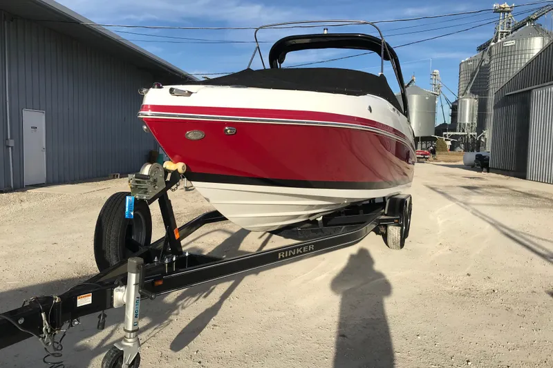 Slide: The Image of 2018 Rinker QX26 BR boat on trailer, parked outdoors near industrial buildings. - 2