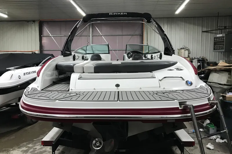 Slide: The Image of 2018 Rinker QX26 BR boat in a garage, showcasing rear deck and seating area. - 25