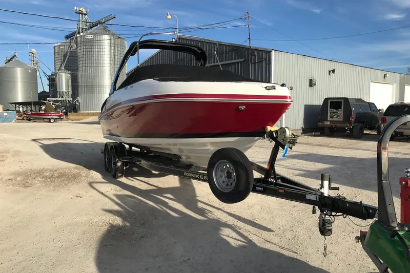 Slide: The Image of 2018 Rinker QX26 BR boat on trailer, parked near industrial buildings. - 3