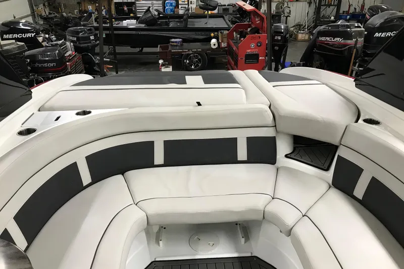 Slide: The Image of 2018 Rinker QX26 BR boat interior with white and gray seating in a workshop setting. - 6