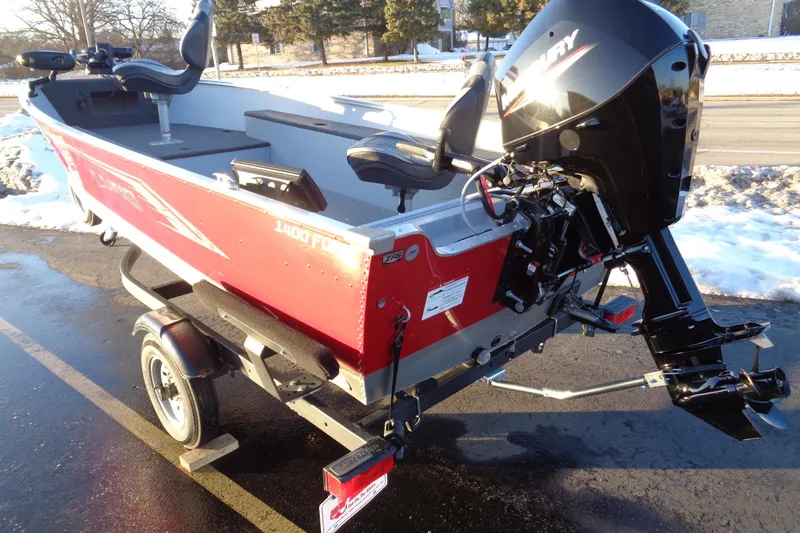 Slide: The Image of 2024 Lund 1400 Fury Tiller boat on trailer, red exterior, parked on snowy pavement. - 11