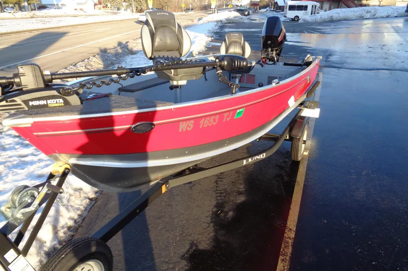 Slide: The Image of 2024 Lund 1400 Fury Tiller boat on trailer, red exterior, parked on snowy roadside. - 2
