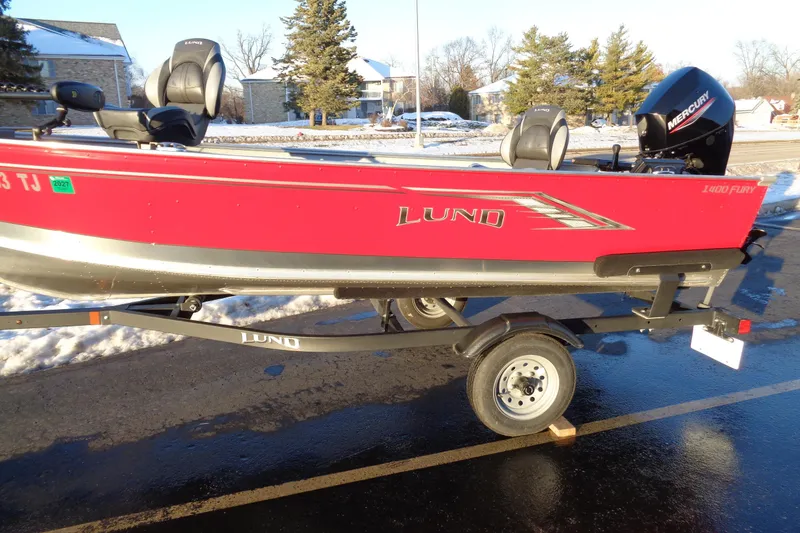 Slide: The Image of 2024 Lund 1400 Fury Tiller boat on trailer, red exterior, parked on snowy pavement. - 4