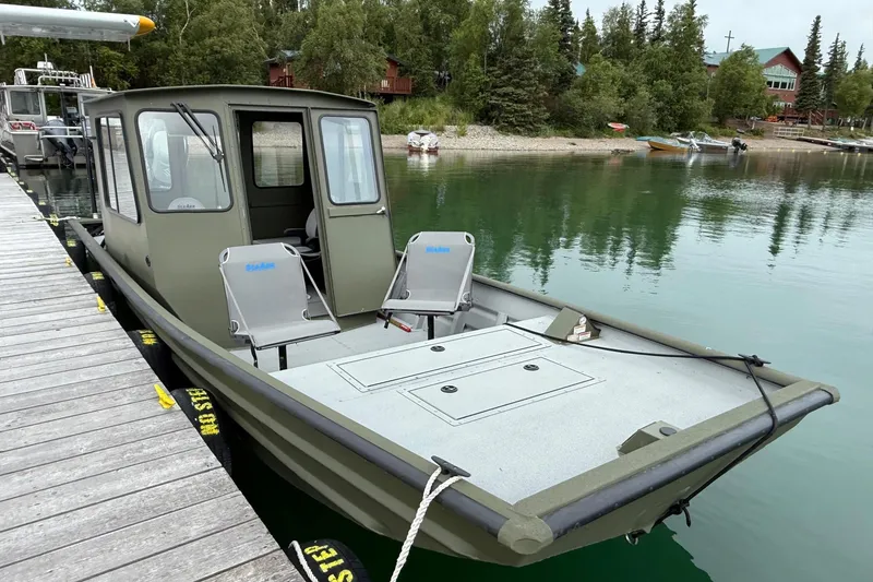 Slide: The Image of 2026 SeaArk 2672 CUB boat docked on calm lake with lush forest backdrop. - 2
