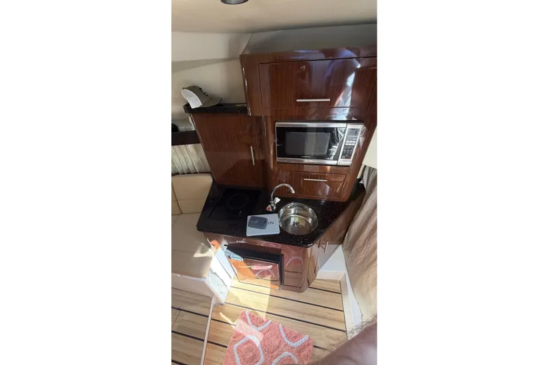Slide: The Image of 2014 Regal 28 Express boat interior kitchen with microwave, sink, and wooden cabinets. - 17