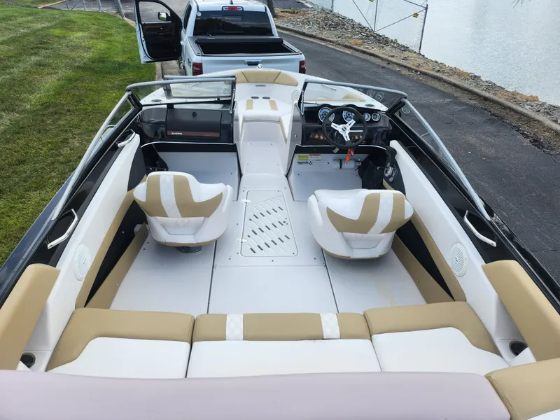 Slide: The Image of 2016 Glastron GT 205 boat interior with beige and white seating, parked near a lake. - 10