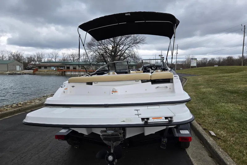 Slide: The Image of 2016 Glastron GT 205 boat with canopy, parked near a lake under cloudy skies. - 2