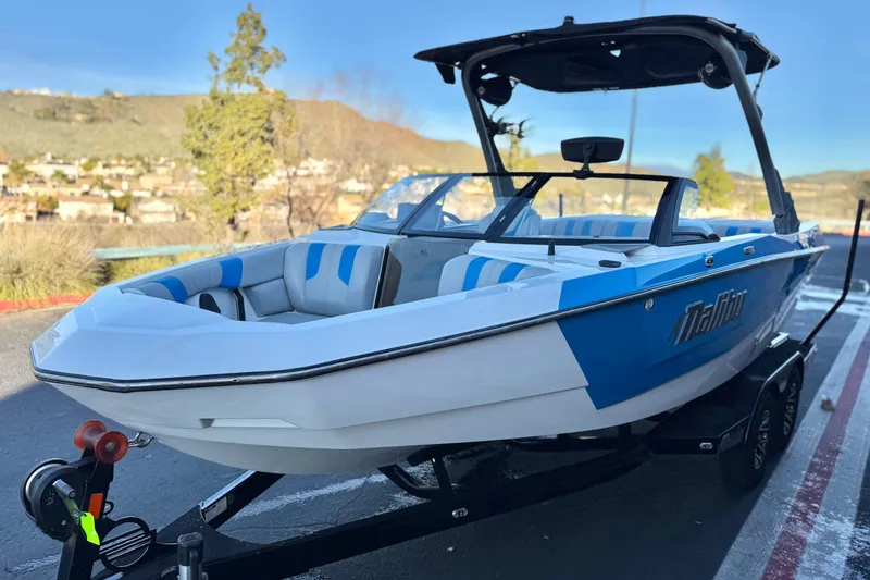 Slide: The Image of 2023 Malibu Wakesetter 21 LX boat with blue and white design on a trailer. - 2