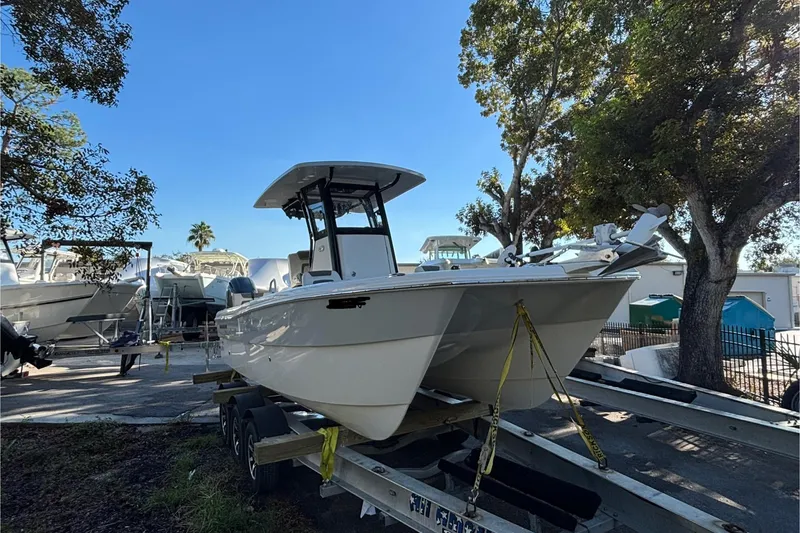 Slide: The Image of 2022 World Cat 235 CC boat on trailer, surrounded by trees and other boats. - 2