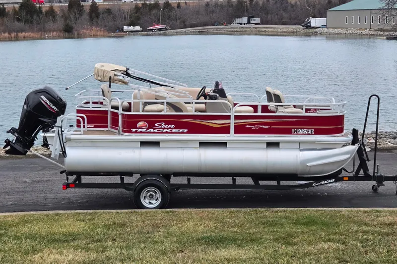The Image of 2020 Sun Tracker Bass Buggy 18 DLX pontoon boat on trailer by a lake. - 0