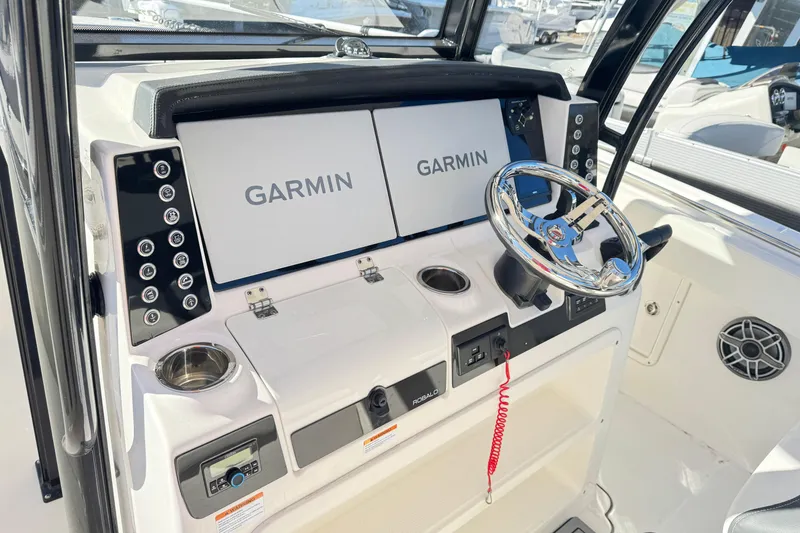 Slide: The Image of 2023 Robalo R302 Center Console boat dashboard with Garmin displays and chrome steering wheel. - 2