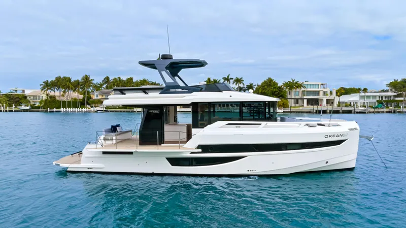 Slide: The Image of A modern 2026 OKEAN 52 boat on calm water, surrounded by palm trees and houses. - 15