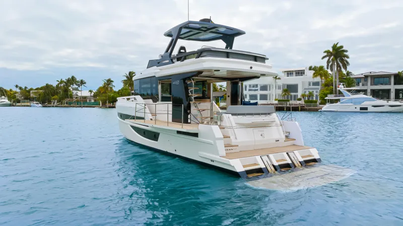 Slide: The Image of The 2026 OKEAN 52 cruises on calm waters, surrounded by palm trees and modern houses. - 29