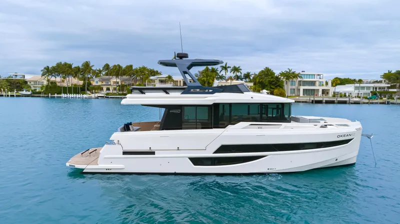 Slide: The Image of The 2026 OKEAN 52 is a sleek motor yacht on calm waters, surrounded by modern homes. - 17