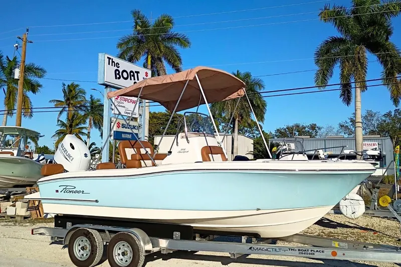 The Image of 2026 Pioneer 202 Sportfish boat on trailer, displayed outdoors with palm trees and dealership signs. - 0