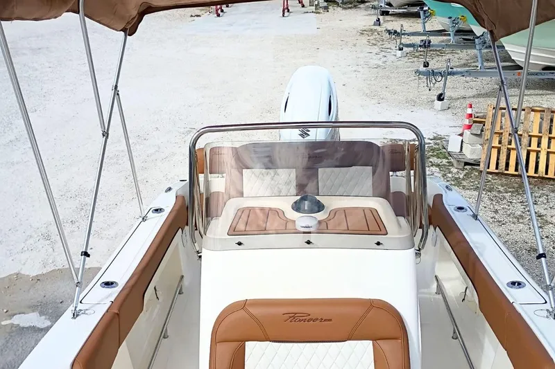 Slide: The Image of 2026 Pioneer 202 Sportfish boat with tan seating and canopy, parked on gravel. - 22