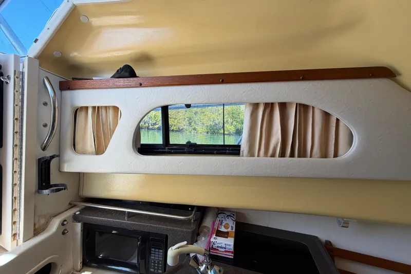 Slide: The Image of 2006 Grady-White Sailfish 282 cabin interior with window, microwave, and beige curtains. - 126