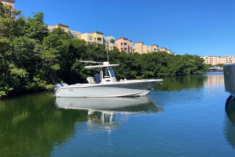 Slide: The Image of 2023 Sea Hunt Gamefish 27 boat on calm water near lush greenery and buildings. - 7