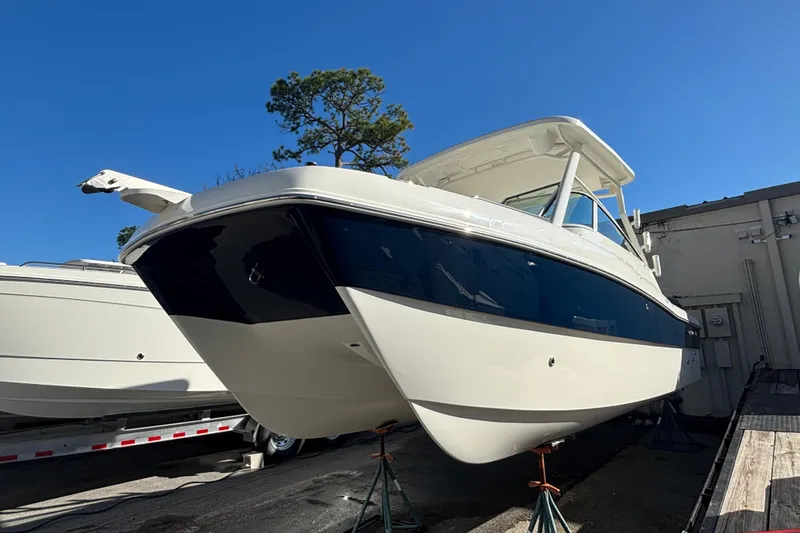 The Image of 2025 World Cat 230 DC boat on stands, blue and white hull, clear sky background. - 0