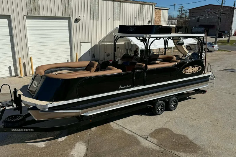 Slide: The Image of 2026 Aloha Paradise 300 Sundeck pontoon boat on trailer, parked outside a warehouse. - 23